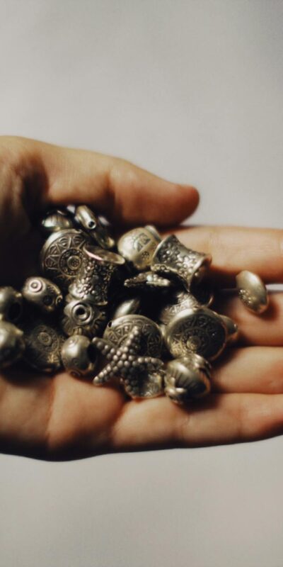 Detailed image of a hand holding intricately designed metal beads with a tattoo visible.